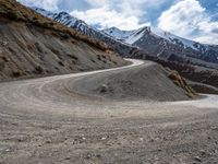 a dirt road winding in the mountains towards some snow - covered mountains and some brown rocks