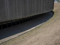 the back wall of a building that has been added to be curved and empty with grass growing out to the ground