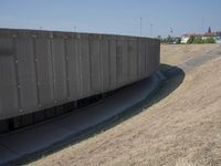 the back wall of a building that has been added to be curved and empty with grass growing out to the ground