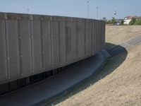the back wall of a building that has been added to be curved and empty with grass growing out to the ground