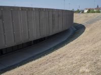 the back wall of a building that has been added to be curved and empty with grass growing out to the ground