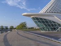 a curved building with a glass front next to another building in a city park area