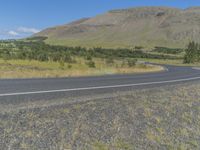 a curved highway in the distance is bordered by lush greenery with a mountain behind it