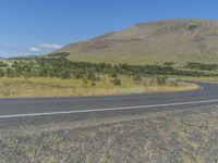 a curved highway in the distance is bordered by lush greenery with a mountain behind it