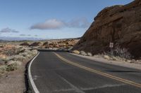 a single curved highway curves past the rock formation that is covering a desert side slope