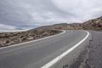 a curved highway in the middle of a rocky hill with a cloudy sky above it