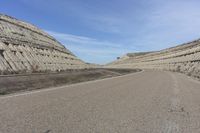 a curved highway curves around a formation of rock walls and sand dunes on an otherwise empty road