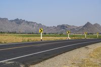 a single lane road has signs indicating yellow and white along with some mountains in the distance