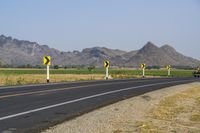 a single lane road has signs indicating yellow and white along with some mountains in the distance