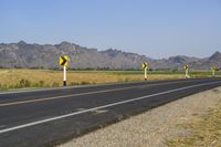 a single lane road has signs indicating yellow and white along with some mountains in the distance