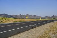 a single lane road has signs indicating yellow and white along with some mountains in the distance