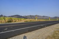 a single lane road has signs indicating yellow and white along with some mountains in the distance