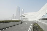 a view of a curved building across a city street with grass in front of it