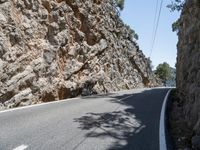 a long curved mountain road with rock walls in the background and trees on either side