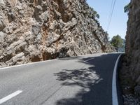 a long curved mountain road with rock walls in the background and trees on either side