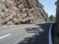 a long curved mountain road with rock walls in the background and trees on either side