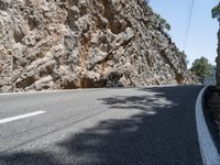 a long curved mountain road with rock walls in the background and trees on either side