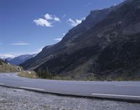 the curved mountain road curves around a rocky mountain range to pass through the valley to an open valley and a blue sky