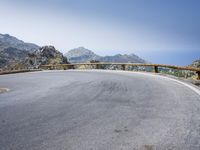 a curved mountain road on the side of a mountain with hills in the background with a blue sky