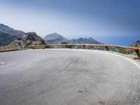 a curved mountain road on the side of a mountain with hills in the background with a blue sky