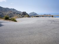 a curved mountain road on the side of a mountain with hills in the background with a blue sky