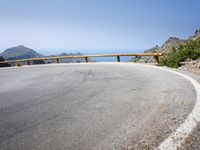 a curved mountain road on the side of a mountain with hills in the background with a blue sky