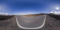 the curved roadway of a mountain road has a clear sky above it and a few clouds