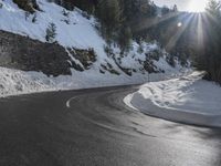 a curved mountain road winds around in the snow with trees, rocks, and rocks,