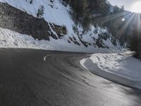 a curved mountain road winds around in the snow with trees, rocks, and rocks,