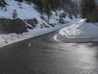 a curved mountain road winds around in the snow with trees, rocks, and rocks,