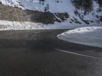 a curved mountain road winds around in the snow with trees, rocks, and rocks,