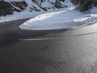 a curved mountain road winds around in the snow with trees, rocks, and rocks,