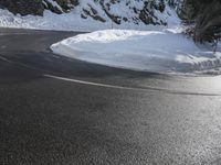 a curved mountain road winds around in the snow with trees, rocks, and rocks,
