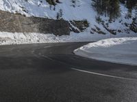 a curved mountain road winds around in the snow with trees, rocks, and rocks,