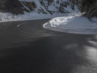 a curved mountain road winds around in the snow with trees, rocks, and rocks,