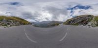 a curved road with mountains and hills in the background on a cloudy day from a fisheye lens