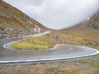 a curved road runs up the mountain side as it reaches a hill with some grass and rocks