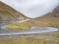 a curved road runs up the mountain side as it reaches a hill with some grass and rocks