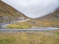 a curved road runs up the mountain side as it reaches a hill with some grass and rocks