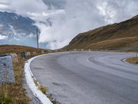 an empty curved roadway with mountains in the background with clouds and mountains in the background