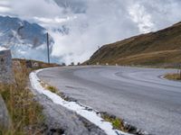 an empty curved roadway with mountains in the background with clouds and mountains in the background