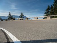 a curved road with a wooden bench next to it and mountains in the distance on a sunny day