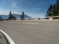 a curved road with a wooden bench next to it and mountains in the distance on a sunny day