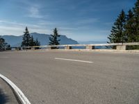 a curved road with a wooden bench next to it and mountains in the distance on a sunny day