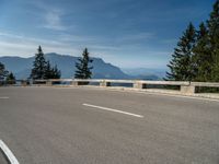 a curved road with a wooden bench next to it and mountains in the distance on a sunny day