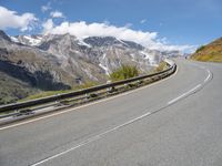 a curved road surrounded by mountains and clouds with a person riding a skateboard on the side