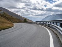 a winding road running through the mountains and hills with a long curved guard rail near it