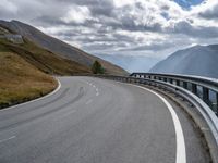 a winding road running through the mountains and hills with a long curved guard rail near it