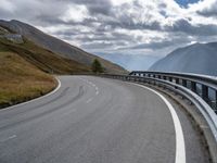 a winding road running through the mountains and hills with a long curved guard rail near it