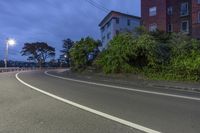 a curved road that is between buildings and trees on a cliff side side at night